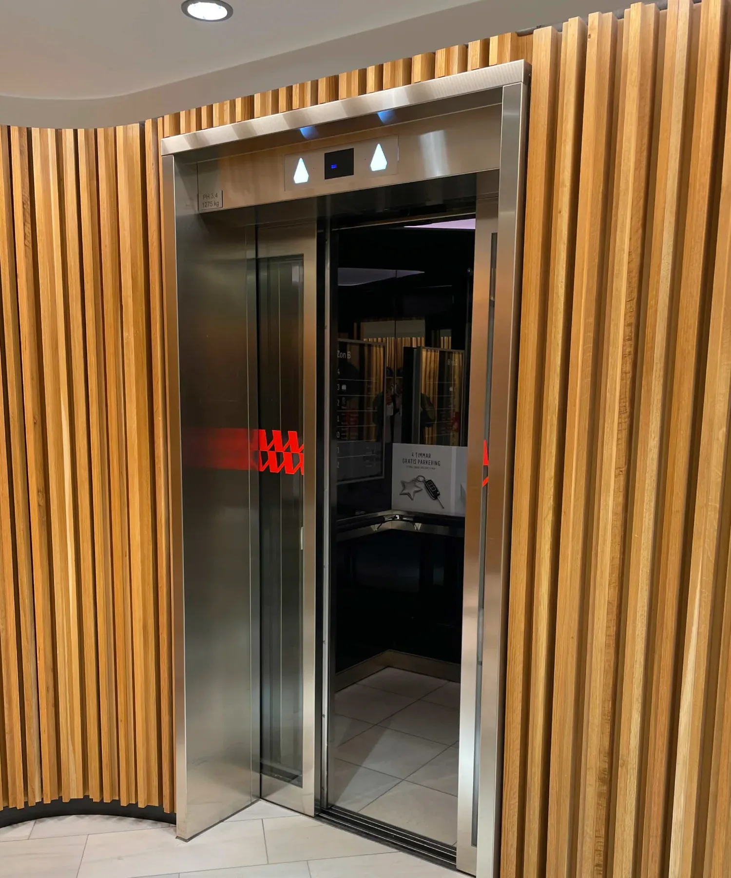 Öppen hiss med rostfri omfattning mellan träribbor, Mall of Scandinavia